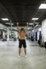 Обратный вид полного тела сильного молодого мускулистого спортсмена в спортивной одежде, поднимающего штангу во время интенсивной тренировки в современном тренажерном зале — стоковое фото