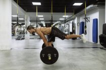 Вид сбоку на все тело сильного молодого мускулистого спортсмена в спортивной одежде, поднимающего штангу во время интенсивной тренировки в современном тренажерном зале — стоковое фото