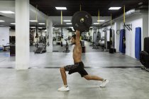 Vista lateral do corpo inteiro de forte jovem atleta masculino muscular em activewear levantando sinos durante o treino intenso no ginásio moderno — Fotografia de Stock