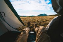 Посев неузнаваемый мужчина-путешественник в повседневной одежде, лежащий в палатке кемпинга и любуясь живописным горным пейзажем в солнечный день — стоковое фото
