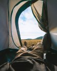 Врожай невпізнаваний чоловік мандрівник у повсякденному одязі лежить у наметі для кемпінгу та захоплюється мальовничим гірським пейзажем у сонячний день — стокове фото