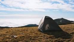 Picturesque scenery of camping tent placed on grassy hill slope in snowy mountainous valley against cloudy sky in sunlight — Stock Photo