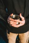 Anonymous young trendy male hiker in warm outfit drinking mug of hot beverage while recreating in camping tent on sunny day — Stock Photo