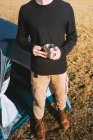 Anonymous young trendy male hiker in warm outfit drinking mug of hot beverage while recreating in camping tent on sunny day — Stock Photo