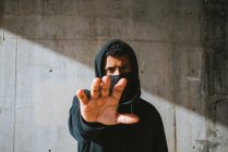 Junger Mann in Kapuzenpulli und Maske steht auf der Straße in der Nähe einer Betonmauer und gibt die Hand — Stockfoto
