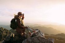 Боковой вид неузнаваемого туриста, сидящего на камне и наблюдающего удивительные пейзажи горной долины в солнечный день — стоковое фото