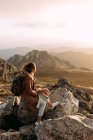 Vista lateral de un excursionista irreconocible sentado en piedra y observando increíbles paisajes del valle de las tierras altas en un día soleado - foto de stock