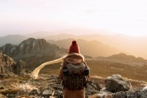 Обратный вид на неузнаваемого туриста, стоящего на камне и наблюдающего удивительные пейзажи горной долины в солнечный день — стоковое фото