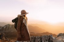 Side view of unrecognizable hiker standing on stone and observing amazing scenery of highlands valley on sunny day — Stock Photo