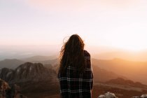 Back view of unrecognizable hiker in blanket standing on stone and observing amazing scenery of highlands valley on sunny day — Stock Photo