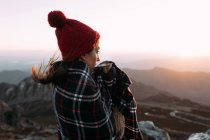 Vista laterale di escursionista in coperta bere caffè caldo e in piedi sulla pietra e osservare paesaggi incredibili della valle degli altopiani nella giornata di sole — Foto stock
