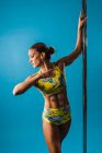 Jovem atleta feminina descalça em bodysuit realizando pose no bastão de dança e olhando para baixo durante o treinamento — Fotografia de Stock