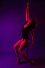 Young female athlete in erotic bodysuit dancing with closed eyes near pole on purple background — Stock Photo
