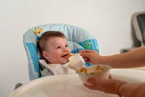 Liebenswertes glückliches Kind mit Lätzchen, das im Kinderwagen sitzt und von Mutter mit süßer Babynahrung gefüttert wird — Stockfoto