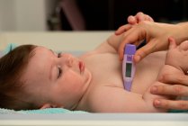 Crop amorevole madre misurazione della temperatura del bambino carino e mettendo termometro in ascella bambino con attenzione — Foto stock