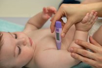Ernteliebende Mutter misst Temperatur des süßen Babys und legt Thermometer sorgfältig in Babyunterarm — Stockfoto