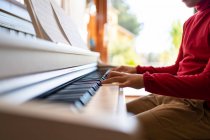 Анонимный ребенок, играющий на пианино, читая ноты и репетируя песню дома — стоковое фото
