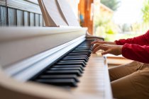 Обрізана анонімна дитина грає на фортепіано, читаючи нотатки та репетируючи пісню вдома — стокове фото
