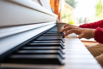 Bambino anonimo ritagliato che suona il pianoforte mentre legge le note e prova la canzone a casa — Foto stock