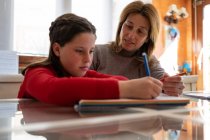 Madre che aiuta la figlia a fare i compiti mentre è seduta a tavola con il quaderno e studia a casa — Foto stock