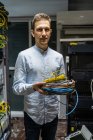 Улыбающийся человек в беспроводной гарнитуре, стоящий с кабелями в комнате сетевого сервера для обеспечения Интернета и связи — стоковое фото