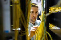 Especialistas masculinos concentrados que trabajan con cables en el servidor mientras administran la red en el centro de datos - foto de stock