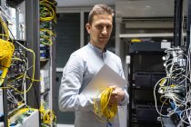 Positiver Mann im Funkkopfhörer mit Netbook und Kabeln im Serverraum — Stockfoto