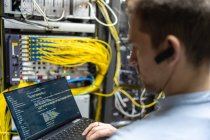 Rückansicht des männlichen Assistenten, der Kabel in Router steckt, während er Laptop zur Überprüfung des Netzwerksystems benutzt — Stockfoto