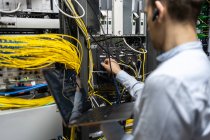 Rückansicht des männlichen Assistenten, der Kabel in Router steckt, während er Laptop zur Überprüfung des Netzwerksystems benutzt — Stockfoto