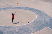 Desde arriba del jugador de baloncesto corriendo con pelota en pista de concreto durante las habilidades de entrenamiento en día soleado - foto de stock