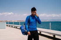 Athlète masculin souriant ayant une conversation sur téléphone portable après l'entraînement sur le remblai de la ville dans la journée ensoleillée — Photo de stock