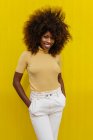 Portrait of a curly haired black woman looking at camera in front of a yellow background — Stock Photo
