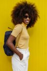 Ritratto di una donna nera dai capelli ricci che guarda la macchina fotografica davanti a uno sfondo giallo — Foto stock