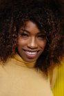 Portrait of a curly haired black woman looking at camera in front of a yellow background — Fotografia de Stock