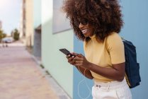 Чорна жінка з афро-волоссям слухає музику на мобільному перед синьою стіною — стокове фото