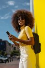 Чорна жінка з афро-волоссям слухає музику на мобільному перед жовтою стіною — стокове фото