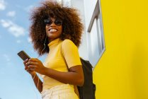 Donna nera con capelli afro che ascolta musica sul cellulare davanti a una parete gialla — Foto stock