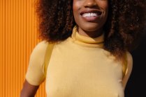 Porträt einer schwarzgelockten Frau, die vor gelbem Hintergrund in die Kamera blickt — Stockfoto