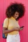 Black woman with afro hair listening to music on mobile in front of a pink wall — Fotografia de Stock
