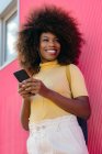 Donna nera con capelli afro che ascolta musica sul cellulare davanti a un muro rosa — Foto stock