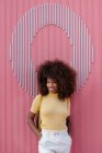 Black woman with afro hair posing in front of a pink wall looking away — Photo de stock
