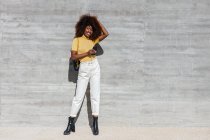 Black woman with afro hair listening to music on mobile in front of a gray wall — Photo de stock