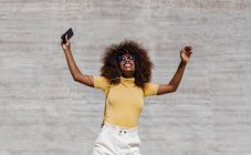 Black woman with afro hair listening to music on mobile in front of a gray wall — Stock Photo