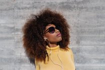 Черная женщина с афроволосами слушает музыку на мобильном телефоне перед серой стеной — стоковое фото