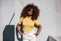 Black woman with afro hair posing in front of a gray wall looking at camera — Photo de stock