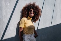 Black woman with afro hair posing in front of a gray wall looking away — Photo de stock
