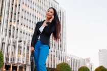From below of Asian female entrepreneur in smart casual style standing in street of downtown and talking on mobile phone while looking away — Stock Photo