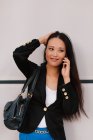 Задоволена азіатська жінка-підприємець говорить на смартфоні, обговорюючи бізнес-проект і озираючись — стокове фото