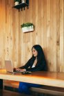 Focalizzata imprenditrice asiatica seduta a tavola nel caffè e digitando su netbook mentre lavorava al progetto online da remoto — Foto stock
