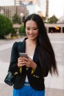 Glückliche asiatische Unternehmerin im smarten lässigen Stil steht in der Straße der Innenstadt und surft auf dem Handy — Stockfoto